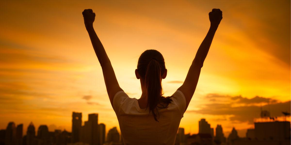 Woman with arms raised at sunrise.