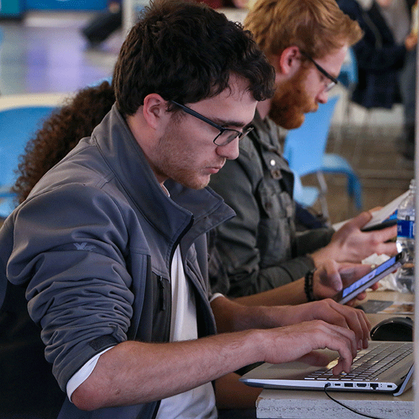 Student typing onto a laptop. Other students in the background.